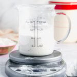 a 2 cup glass measuring cup sits on a silver kitchen scale. the sourdough starter in the cup comes up to the 1 cup line.