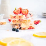 Four lemon berry blondies in a stack with other berries and lemon slices nearby