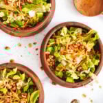 three bowls of lettuce and walnut salad shot overhead. a large wooden spoon sits to the right and a silver fork sits to the left.