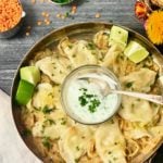 an overhead shot of a skillet filled with dal pierogies. a small bowl of yogurt sauce sits in the center. next to the pan is a small bowl of minced cilantro and a measuring cup of dried pink lentils.