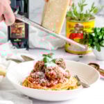 grating parmesan over a bowl of spaghetti
