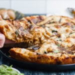 a hand reaching in and pulling an ooey gooey slice of pizza away from the pie