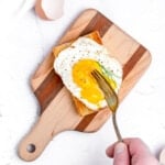 a fork cuts into a runny egg yolk on a fried egg