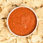 a bowl of salsa in the middle of a bunch of tortilla chips.