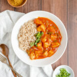 an overhead shot of curry chicken in a bowl to the right of a pile of rice garnished with cilantro