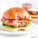 a turkey burger on a bun with bacon, red onion, and havarti cheese with a bite taken out of it