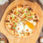 a breakfast pizza cut in half right through an egg yolk which is spilling into the gap on the pizza peel between the two halves.