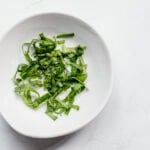an overhead shot of thinly sliced strips of basil in a small white bowl