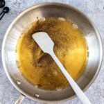 an overhead shot of a stainless steel skillet with melted brown butter. a white silicone spatula is resting in the pan.