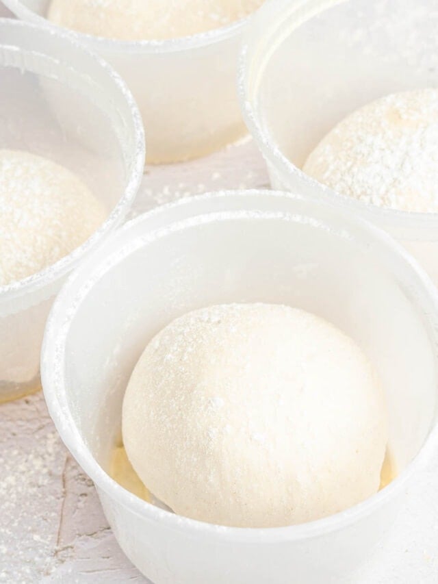 four round deli containers with balls of pizza dough in them.