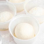 four round deli containers with balls of pizza dough in them.