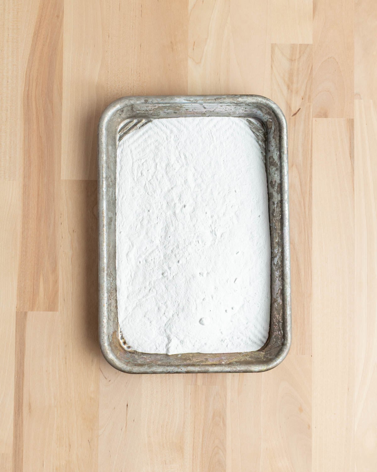 A metal baking tray filled with a layer of baking soda sits on a light wooden surface.