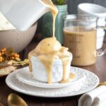 a ramekin with a heaping scoop of mashed potatoes sits on top of two plates. gravy has been poured over the top and is dripping down the sides pooling in the plate below.
