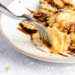 an extreme close up of a fork piercing half of a ravioli on a plate drizzled with balsamic vinegar and brown butter sauce