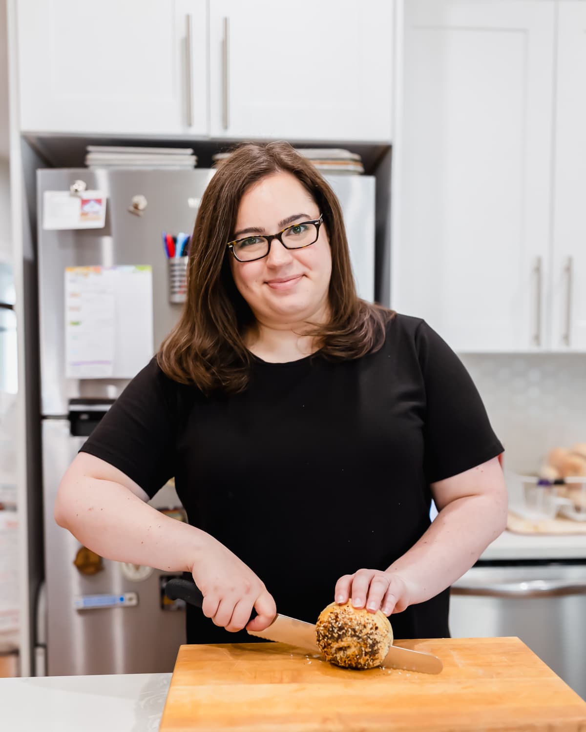 rebecca wearing a black t-shirt using a knife to slice a bagel in half