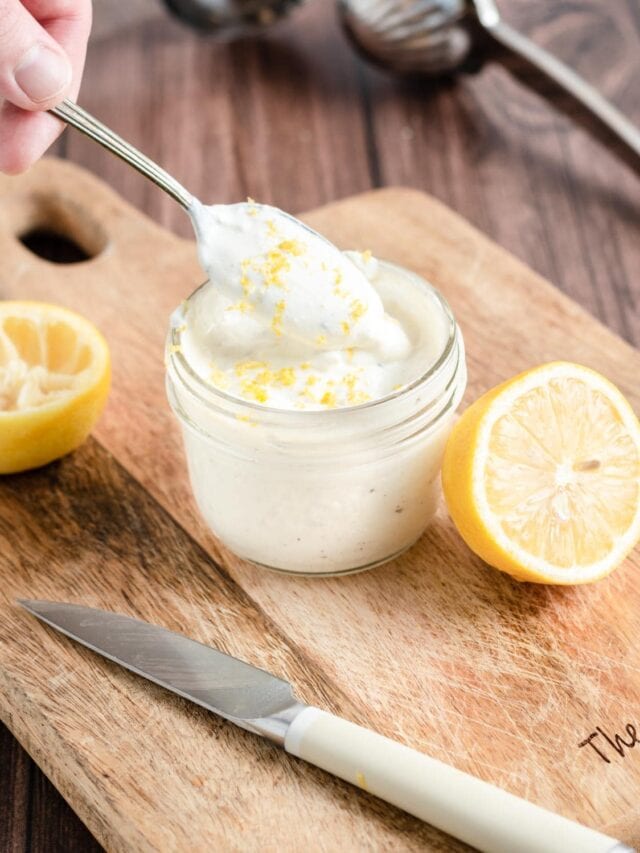 lemon greek yogurt sauce in a small glass jar. a spoon lifts some out of the jar.