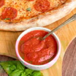 a small bowl of red pizza sauce with a spoon in it.