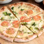 a sliced white pizza topped with tomatoes and broccoli.