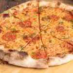 a thin crust pepperoni pizza cut into slices on a pizza peel.