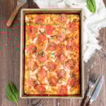 focaccia pizza topped with pepperoni and fresh basil in a rectangular metal pan.