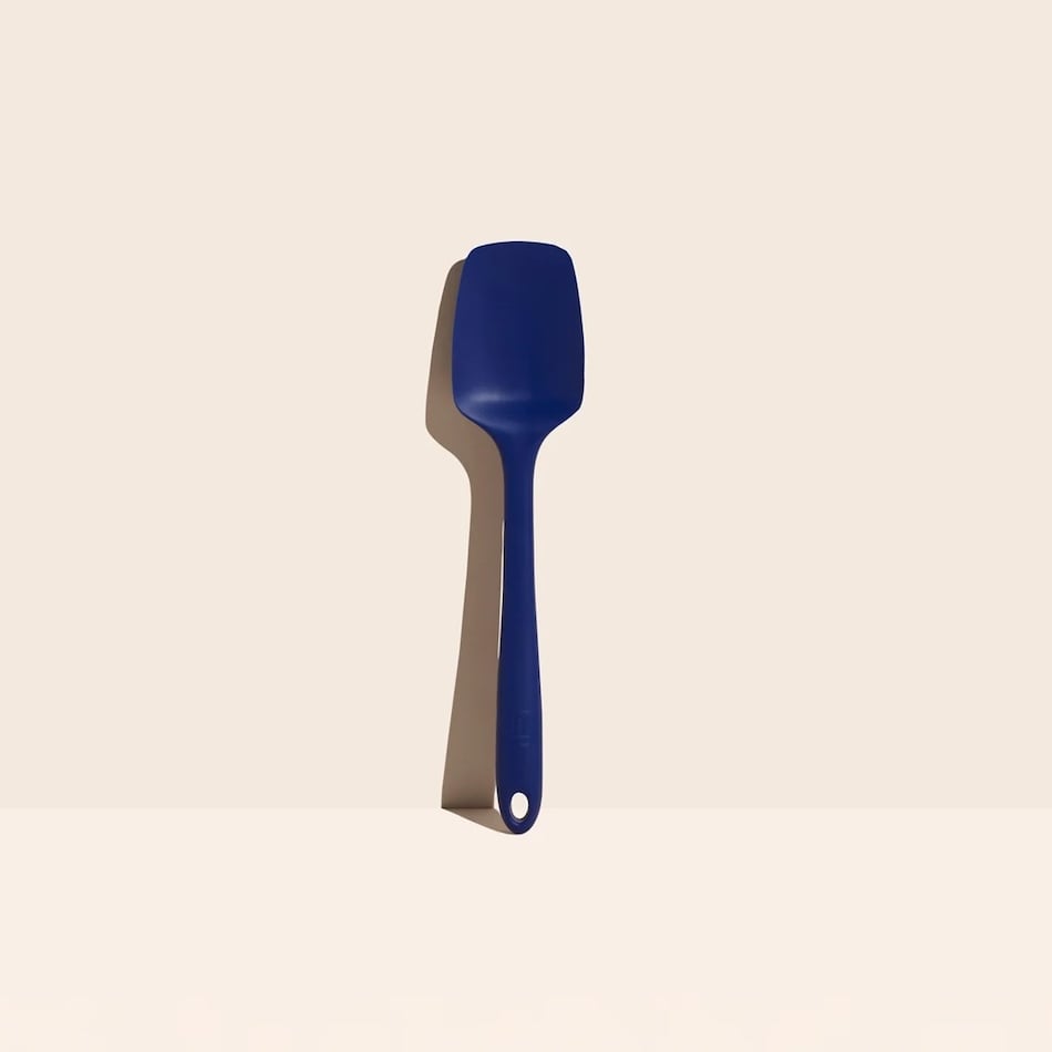 A red silicone spatula with a hole at the end of the handle is standing upright against a plain, light-colored background.