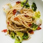 an overhead shot of brussels sprouts carbonara in a white bowl. a fork sticks out of the noodles.