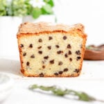 a cross section of a loaf of rosemary chocolate chip cake with a sprig of fresh rosemary in front of it.