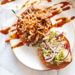 an overhead shot of an open face pulled pork sandwich with a zig zag of bbq sauce over the pulled pork and red onion and coleslaw on the other half of the bun