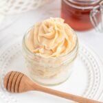fluffy honey butter piped in a rosette in a glass jar. a honey wand is in front of it.