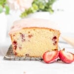 a cross section of a loaf of strawberry pound cake with pink icing on top and two strawberry halves in front of it.