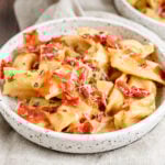 a shallow white bowl with agnolotti topped with crispy prosciutto.
