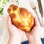 two hands holding a small braided challah bread.