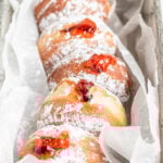 homemade jelly filled donuts lined up in a parchment paper lined metal loaf pan.