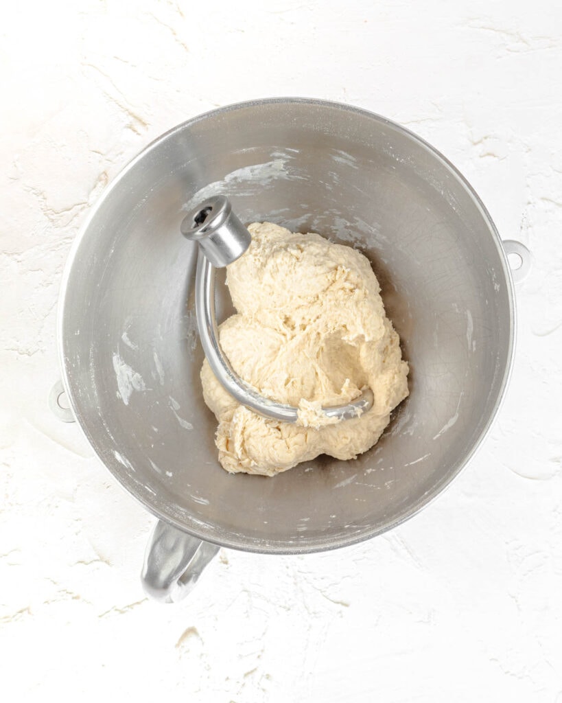 the bread dough after mixing in a stand mixer bowl with a dough hook. the dough is shaggy and rough looking.