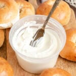 cream cheese in a plastic deli container surrounded by bagels.