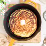 single pancake in a cast iron skillet topped with a pat of butter.