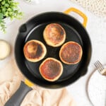 four browned english muffins in a cast iron skillet.