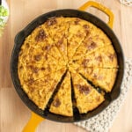 cornbread cut into 12 wedges in a cast iron skillet on a butcher block surface