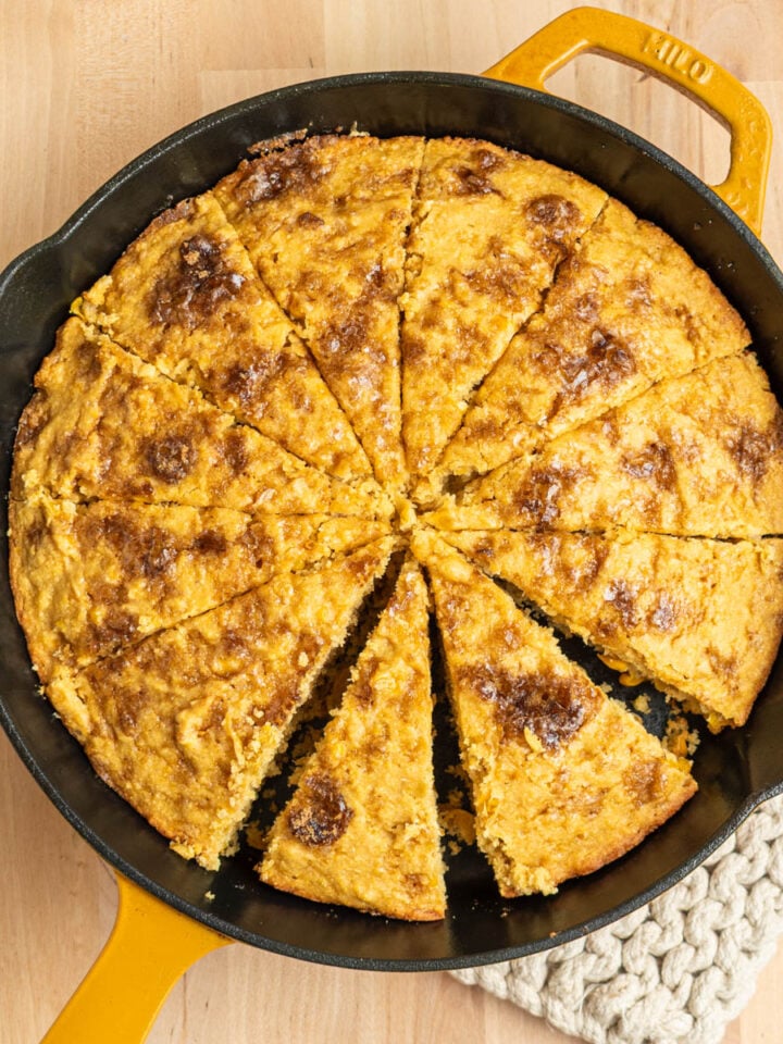 cornbread cut into 12 wedges in a cast iron skillet on a butcher block surface