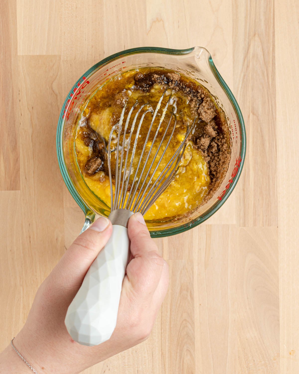 Whisking the wet ingredients, including brown sugar, in a glass liquid measuring cup.