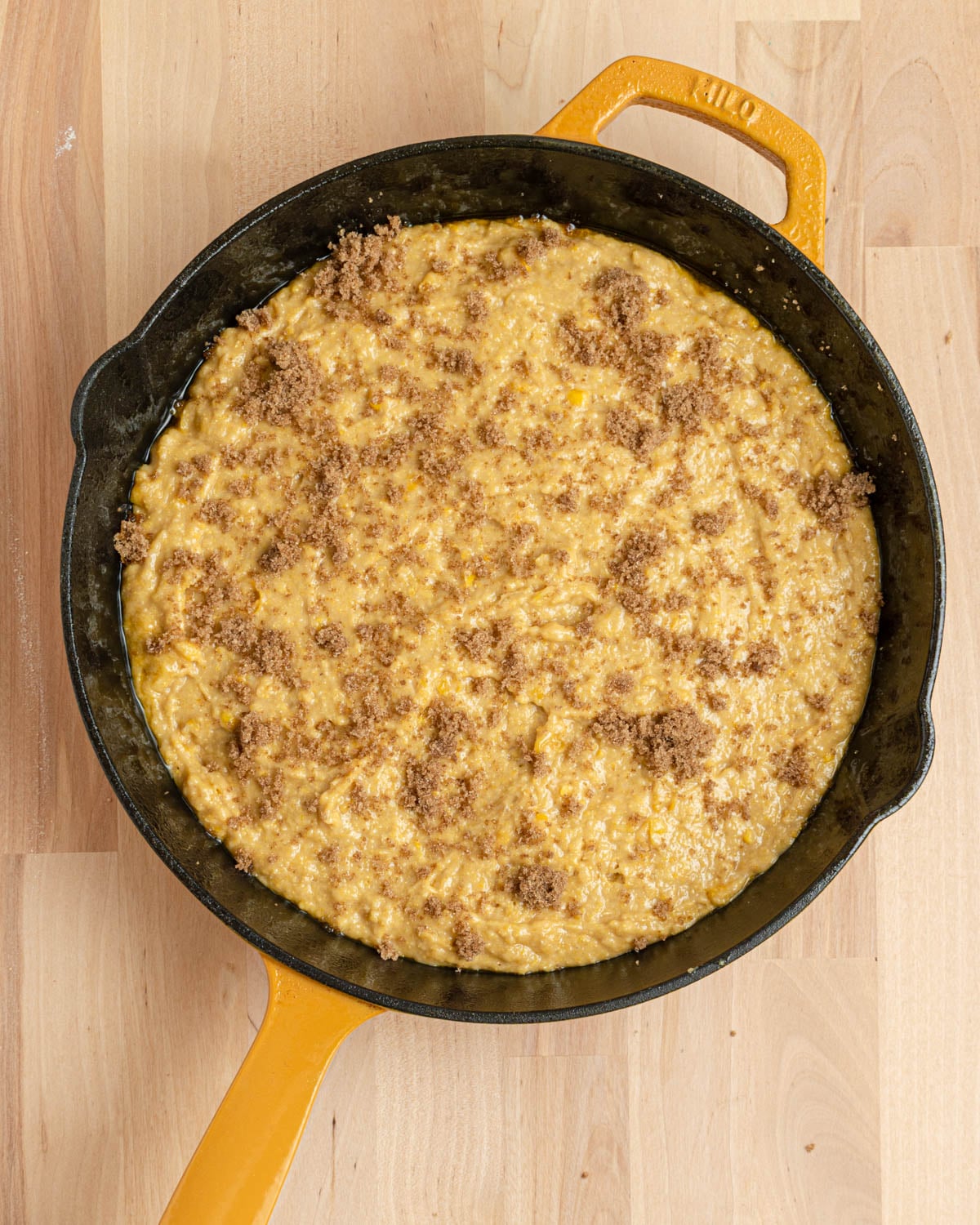 cornbread batter in a cast iron skillet topped with brown sugar before baking.