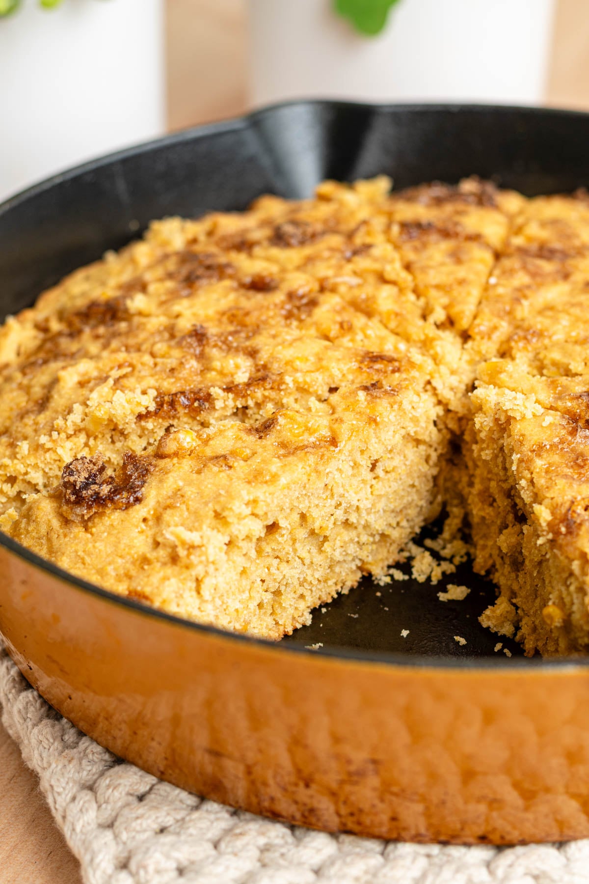 Close up of cornbread in a skillet with a wedge removed showing the inside crumb.
