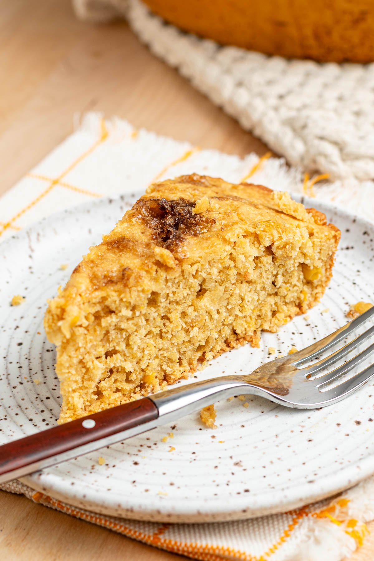 A sliced wedge of cornbread on a white plate with a fork.