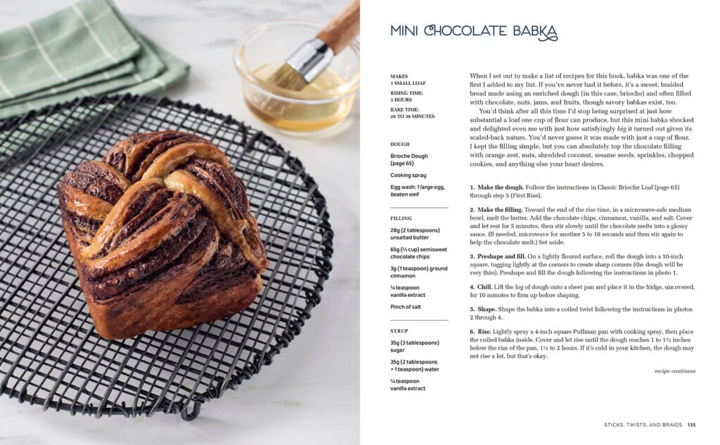A loaf of chocolate babka sits on a round wire cooling rack. Beside it is a glass bowl with a pastry brush, and a green cloth napkin. A recipe for mini chocolate babka appears on the right side of the image.