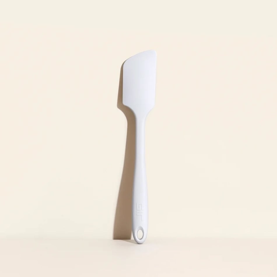 A white silicone spatula with a flat, angled edge is standing upright against a light beige background.