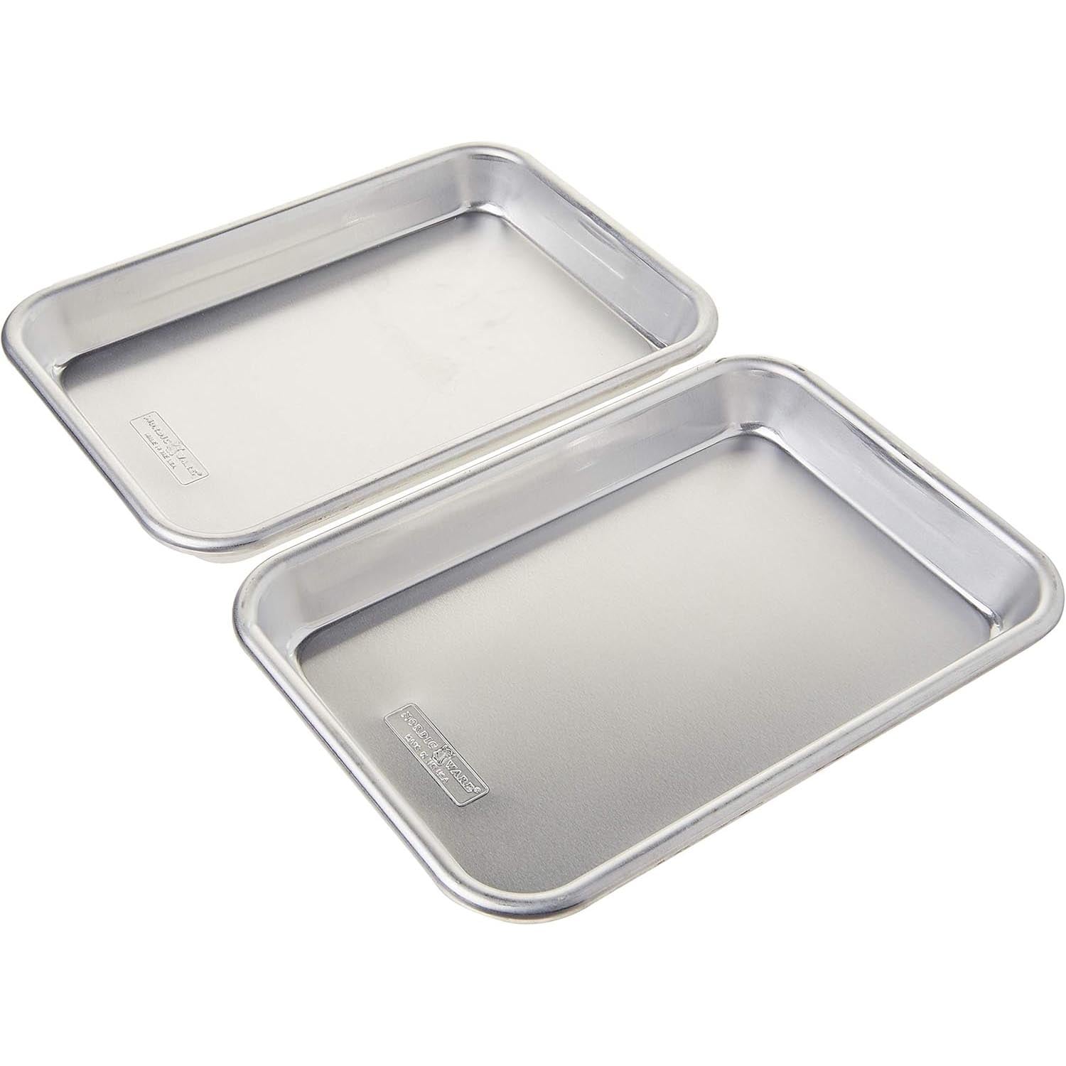 Two rectangular metal baking sheets with raised edges are stacked slightly overlapping on a white background. Both have a smooth, shiny surface and appear unused.