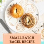 A round plate with illustrations of baked goods holds two bagels, one plain and one seeded. Beside the plate are a serrated knife, a checkered napkin, and white flowers. Text reads: Small Batch Bagel Recipe (Makes 2 Bagels!).