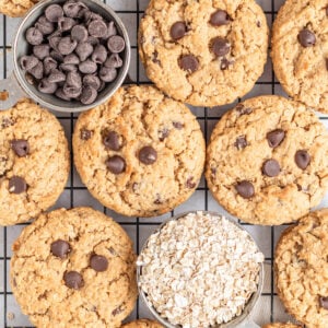 Chocolate chip oatmeal cookies are arranged on a cooling rack with two small bowls—one filled with chocolate chips and the other with rolled oats—giving a cozy, homemade vibe perfect for fans of classic treats like peanut butter cookies.