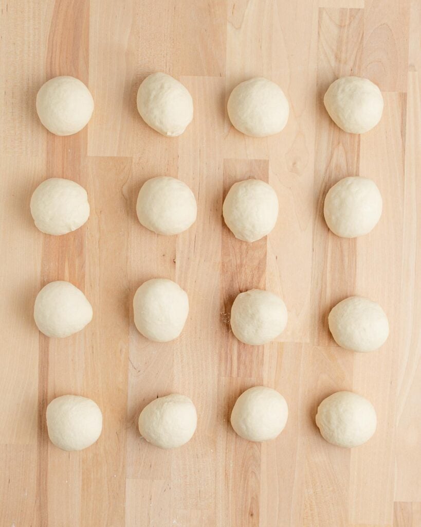 Fifteen evenly spaced dough balls are arranged in a 3 by 5 grid on a light wooden surface.
