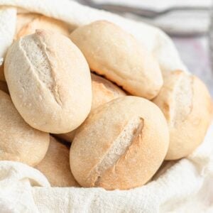 A close-up of several oval-shaped french bread rolls with light brown crusts and slits on top, arranged in a cloth-lined basket.